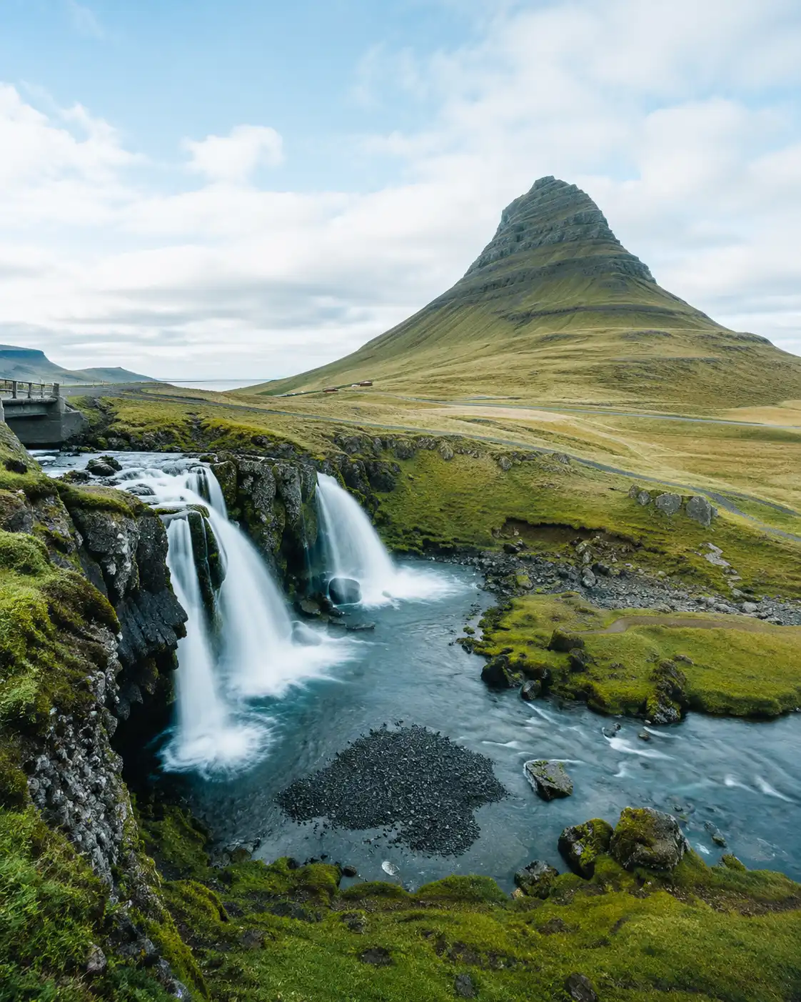 İzlanda’daki Kirkjufell Dağı, ön plandaki Kirkjufellsfoss Şelalesi ve yemyeşil volkanik arazi manzarası.